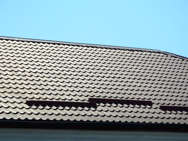 A fragment of a roof from a metal tile of dark red color. Quality Roofing