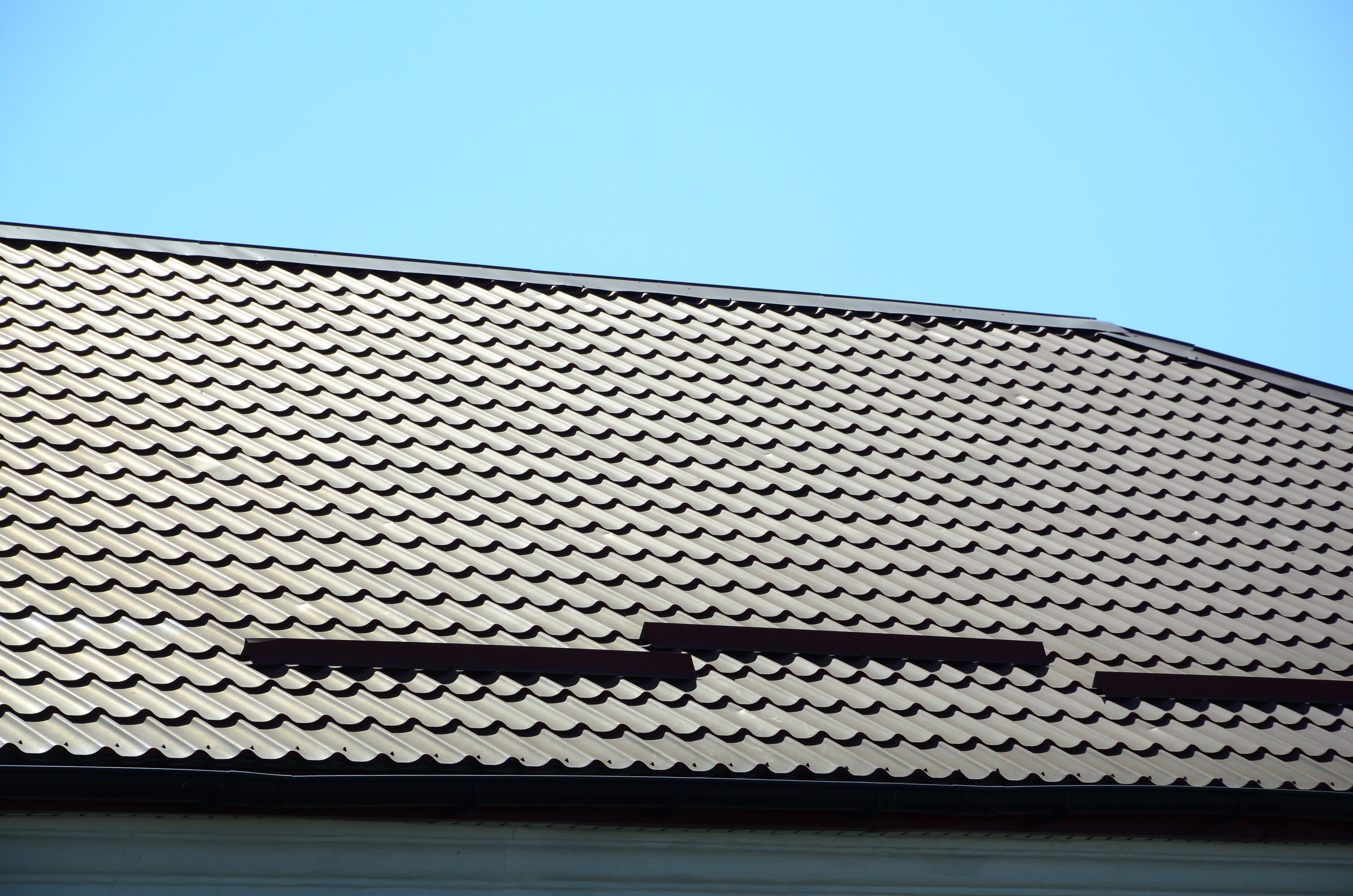 A fragment of a roof from a metal tile of dark red color. Quality Roofing A fragment of a roof from a metal tile of dark red color. Quality Roofing